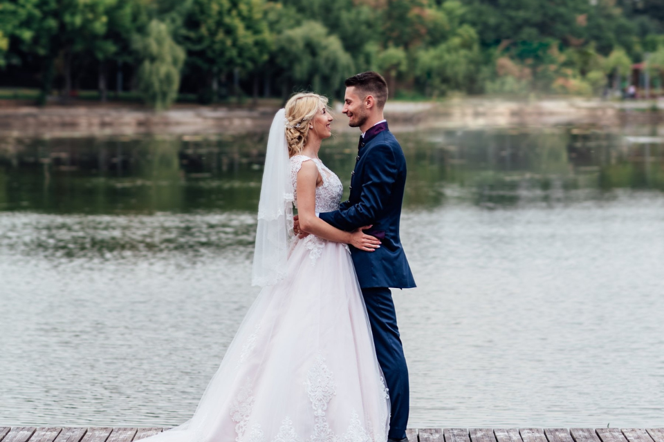 A wedding couple standing on a dock over a lake peering into each other's eyes