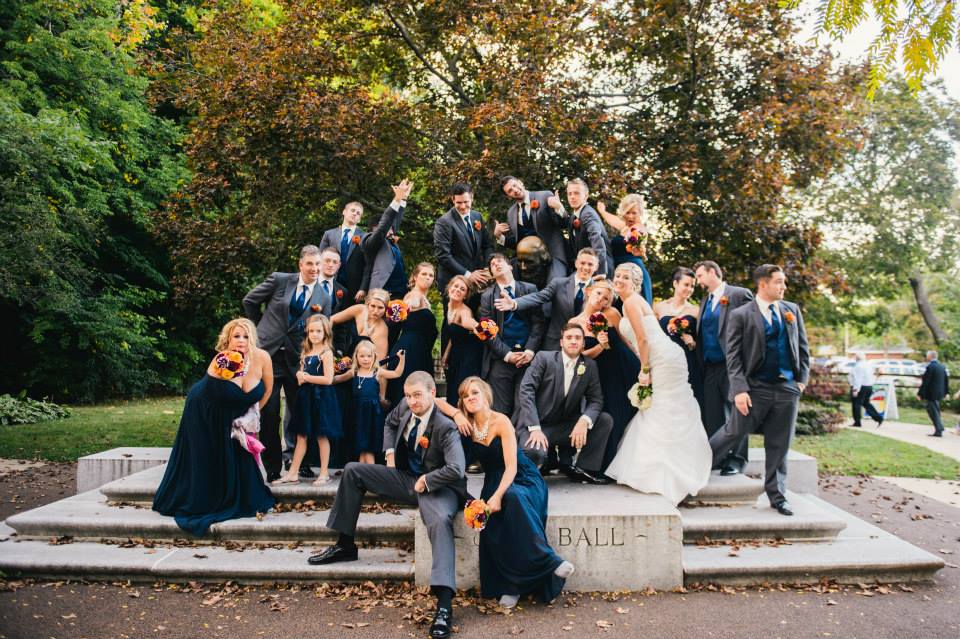 A large group wedding party posing for a photo on top of the John Ball Zoo statue