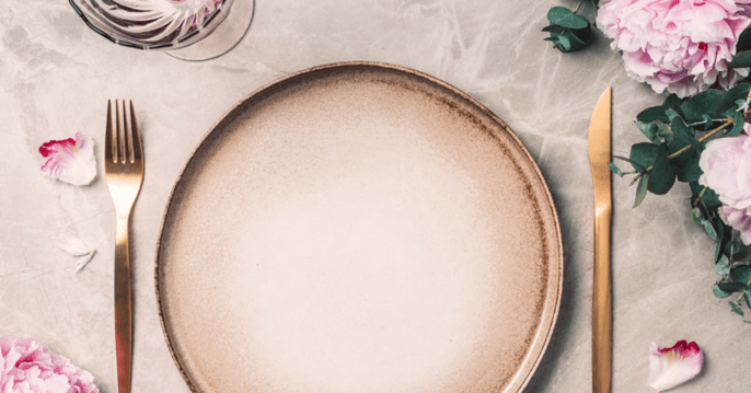 A modern beige plate with gold tinted silverware next to it. Set on top of a velvet tablecloth. 