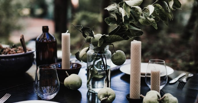 A dark and moody dinner display. There are a lot of greens and dark tones, apples, and dinnerware on the table. 