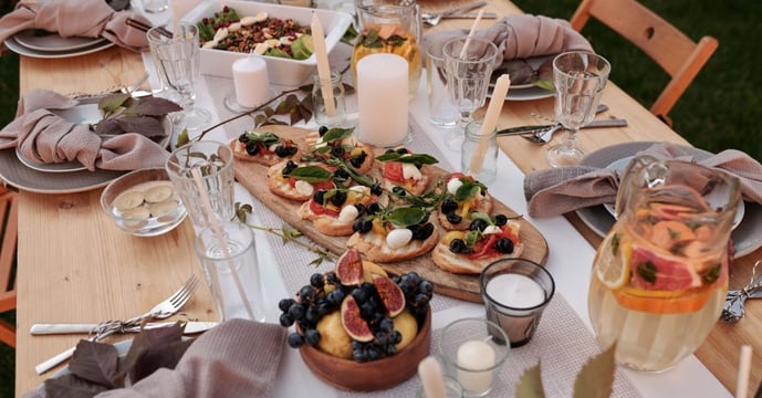 A wooden table that has bread in the middle with fresh cheese and plates. There is a very rustic feeling about the photo.